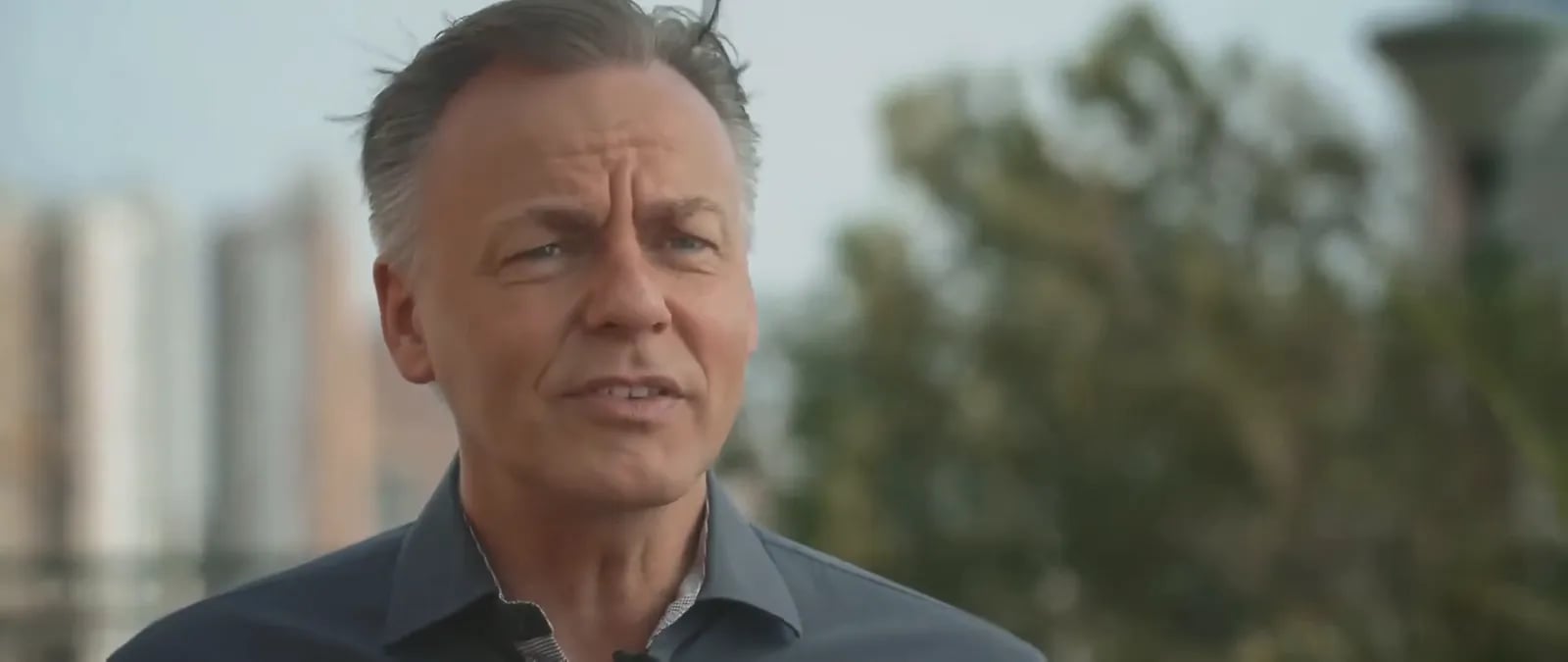 Ein Mann im Interview, hinter ihm unscharf Hochhäuser und Bäume