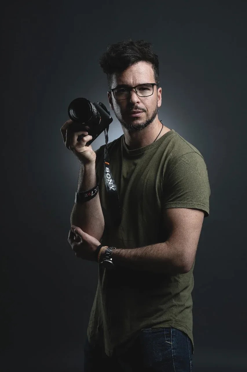 Porträt vor dunklem Hintergrund: ein Mann mit Brille hält eine Sony-Kamera neben das Gesicht und blickt ernst in die Kamera