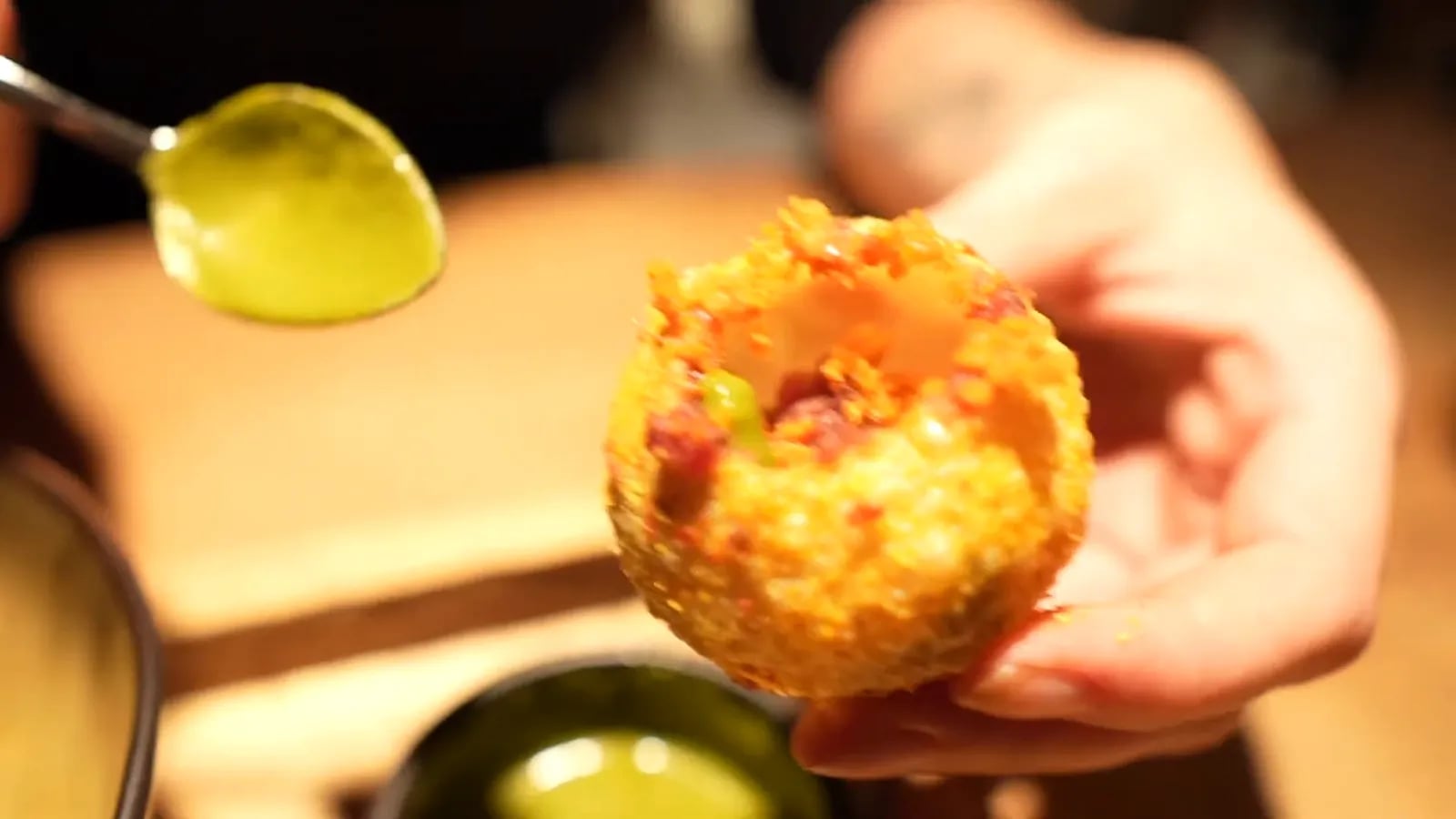 Ein Löffel Kräuteröl über einer frittierten Kugel, in Nahaufnahme