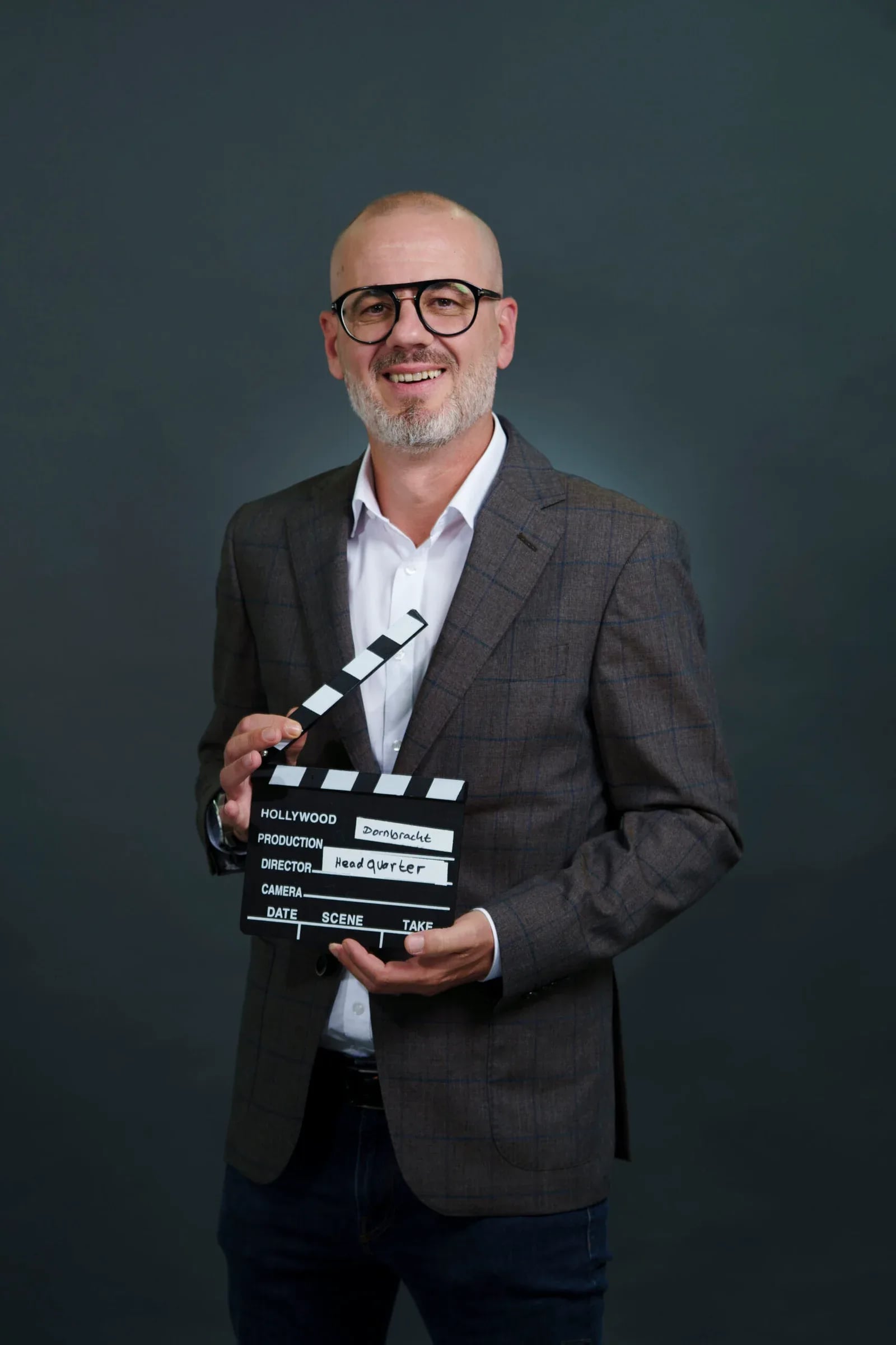 Mitarbeiter mit Brille und kariertem Sakko hält die Filmklappe