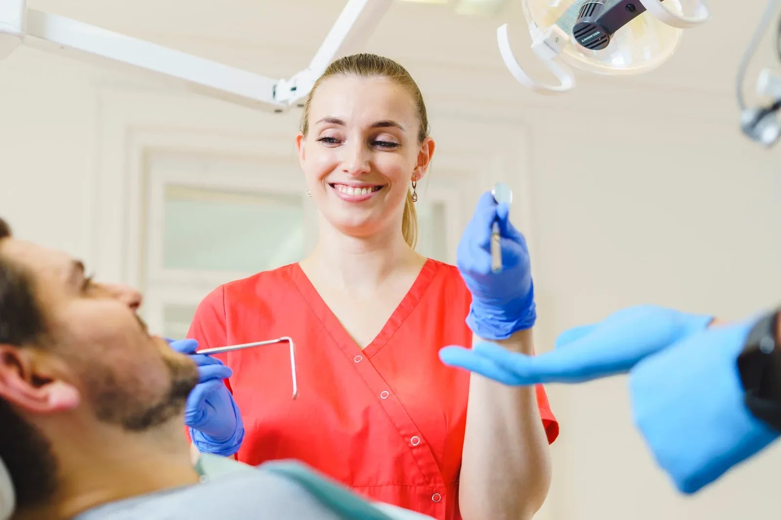 Assistentin reicht ein Instrument an, der Patient lächelt