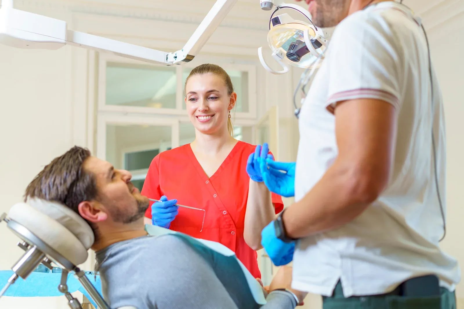 Assistentin und Zahnarzt im Gespräch mit einem Patienten auf dem Behandlungsstuhl